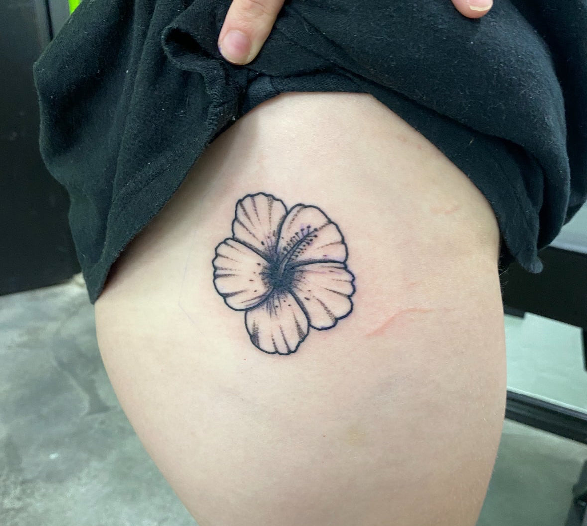 Tattoo of a flower on a person's thigh with a hand holding the skin taut.