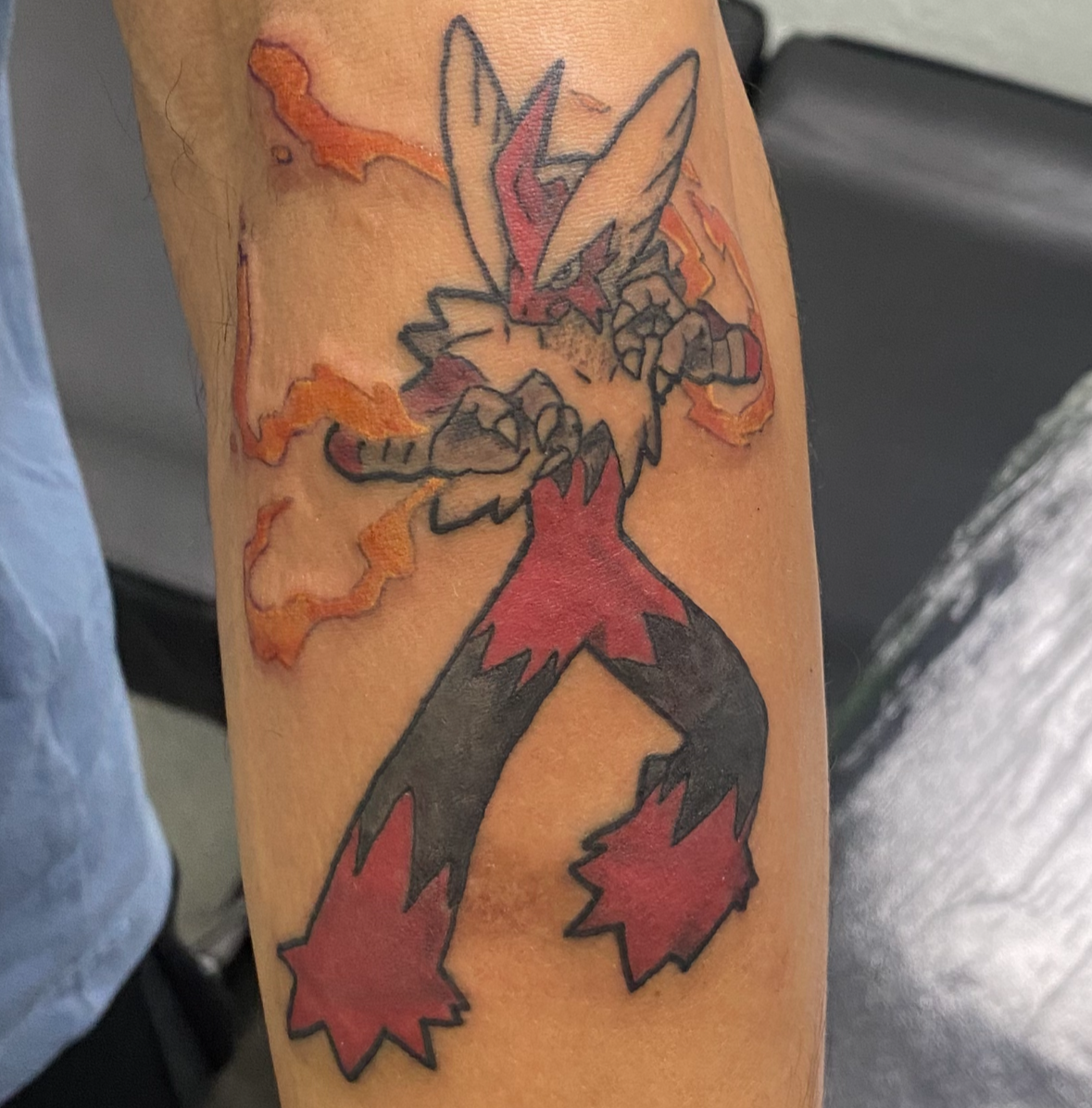 Tattoo of a character with flames on a person's arm, with another tattoo above it.