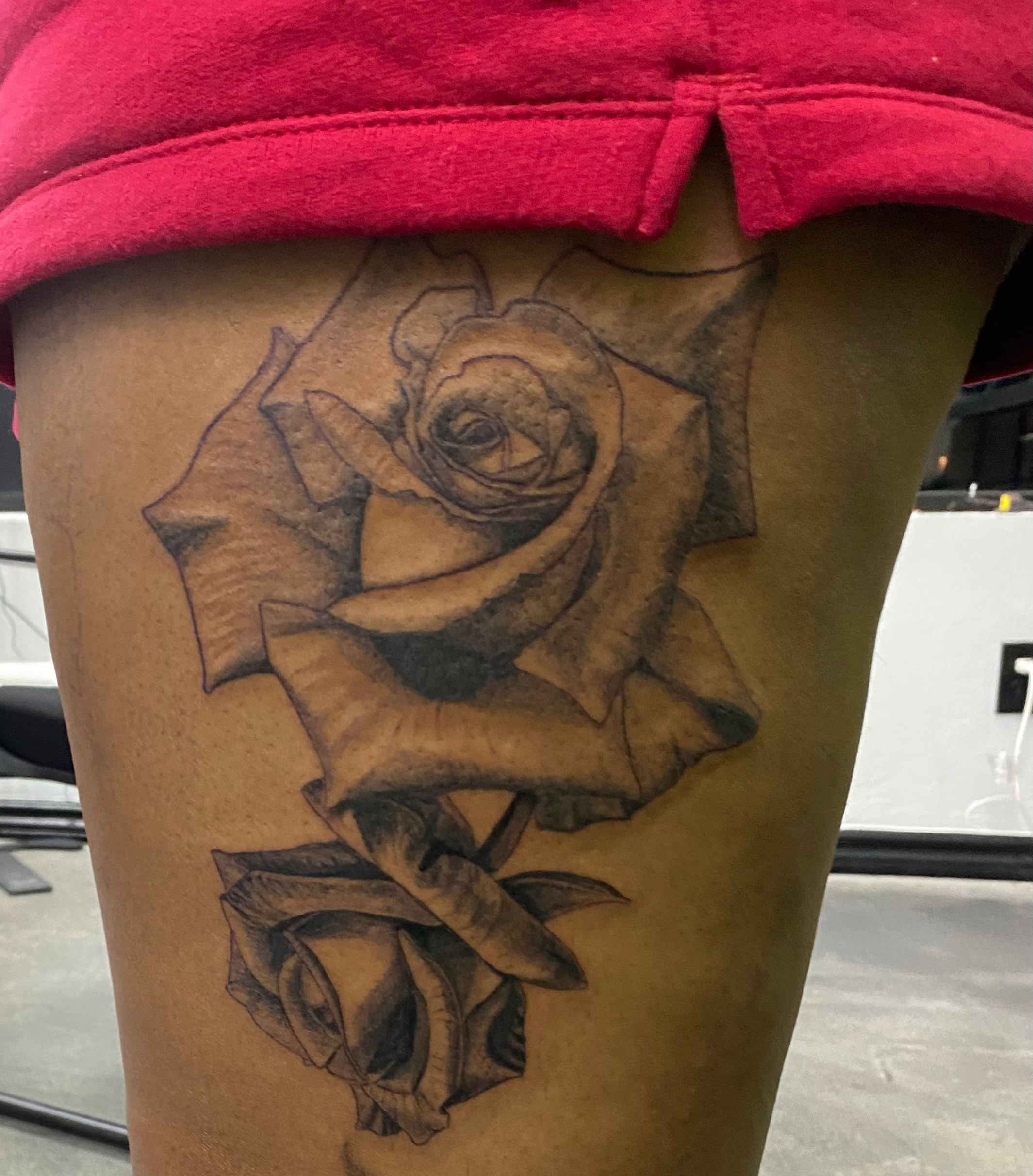 Person with a large rose tattoo on their leg in an indoor setting.